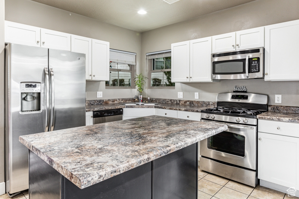 Kitchen with light tile floors, a center island, appliances with stainless steel finishes, white cabinets, and sink