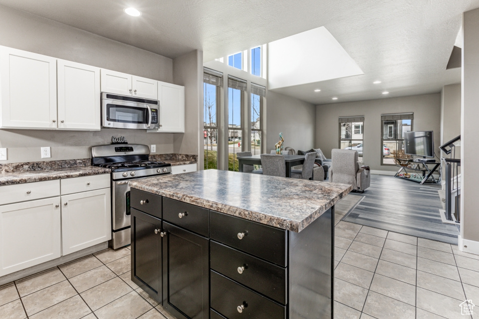 Kitchen featuring appliances with stainless steel finishes, white cabinetry, light tile flooring, and a center island