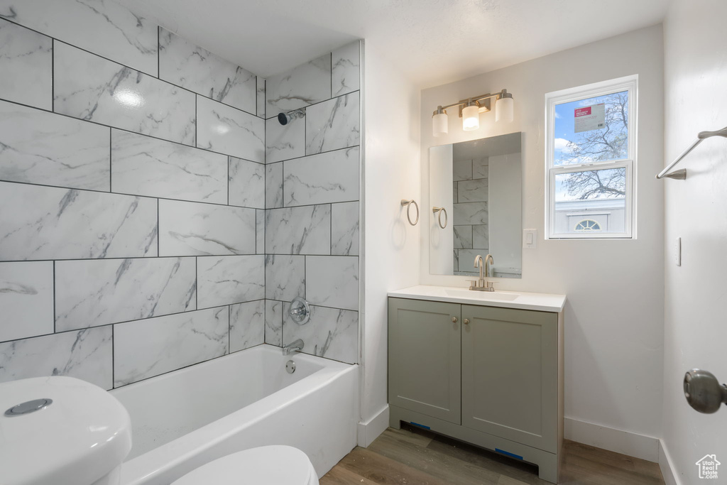 Full bathroom with oversized vanity, toilet, tiled shower / bath, and hardwood / wood-style flooring