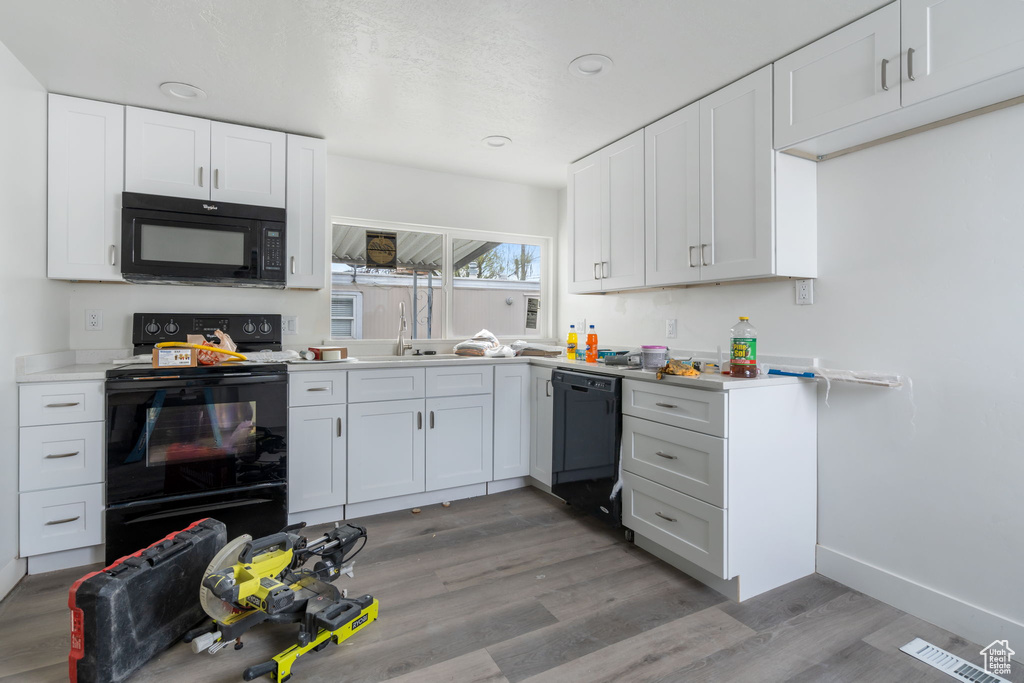 Kitchen featuring white cabinets, sink, black appliances, and dark hardwood / wood-style flooring