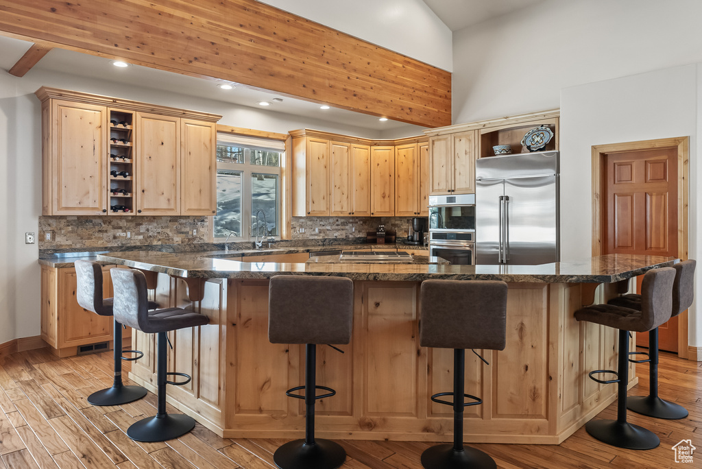Kitchen featuring light brown cabinets, light hardwood / wood-style floors, a breakfast bar, fridge, and backsplash