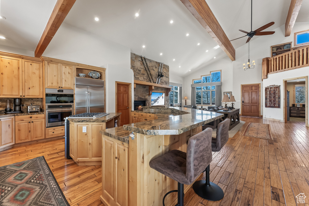 Kitchen with ceiling fan with notable chandelier, a kitchen bar, appliances with stainless steel finishes, light hardwood / wood-style flooring, and a center island