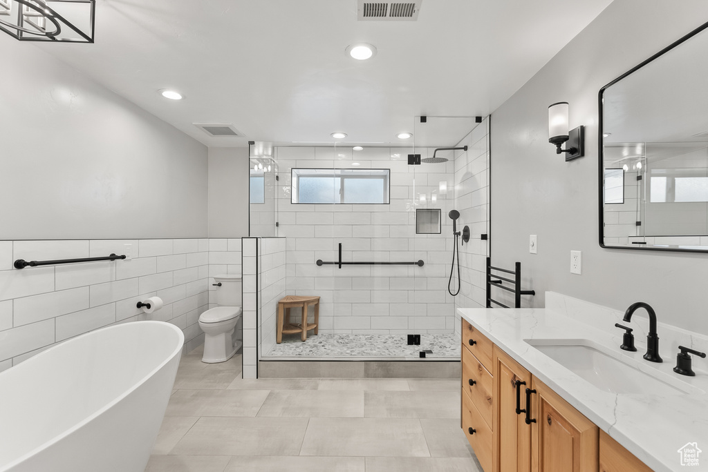 Full bathroom with tile walls, toilet, vanity, tile flooring, and separate shower and tub