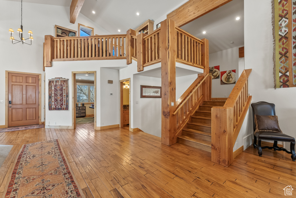Staircase featuring beamed ceiling, light hardwood / wood-style flooring, high vaulted ceiling, and an inviting chandelier
