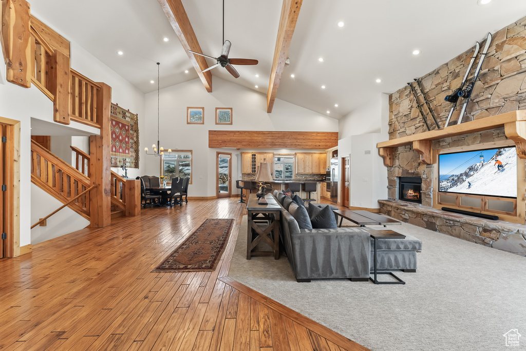 Living room with light hardwood / wood-style floors, high vaulted ceiling, beam ceiling, ceiling fan with notable chandelier, and a stone fireplace