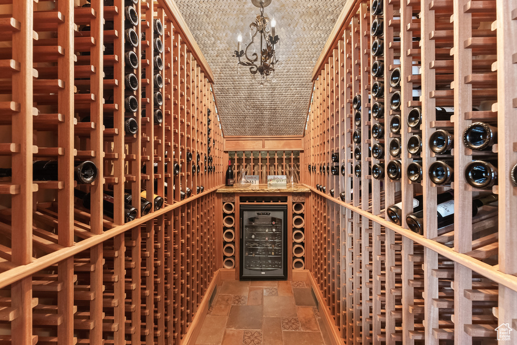 Wine cellar featuring a chandelier, wine cooler, and dark tile flooring