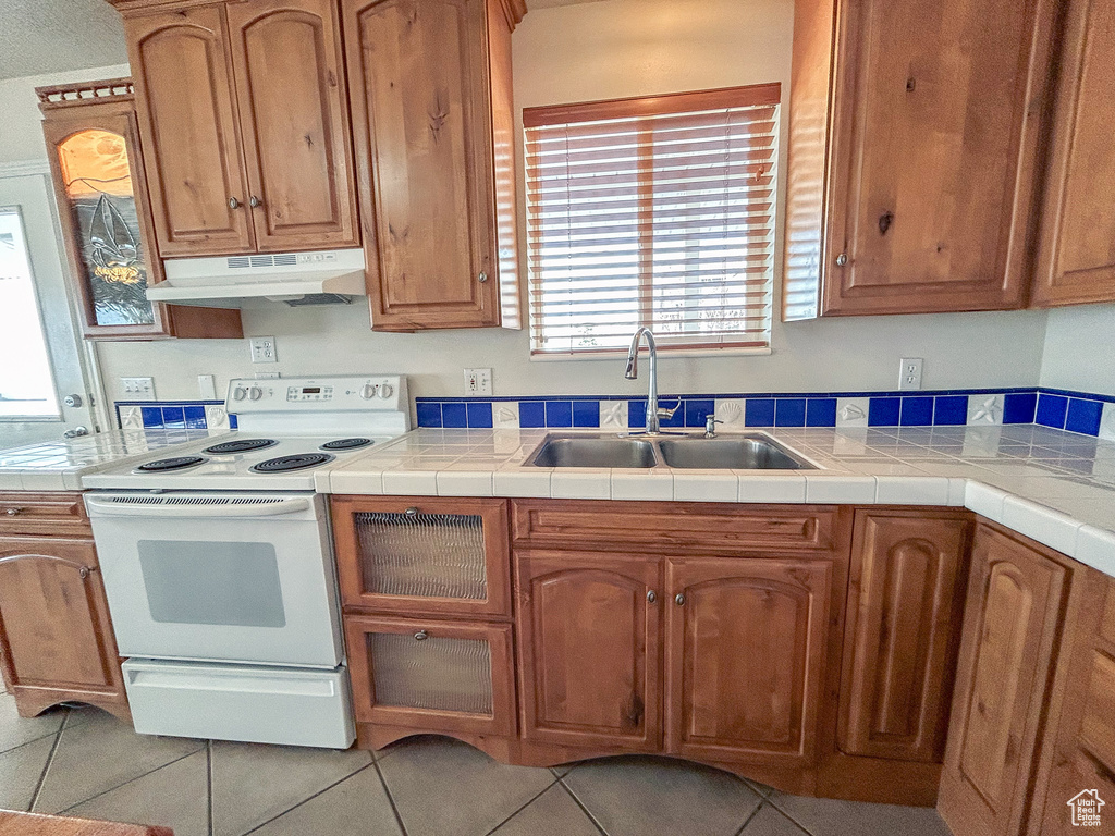 Kitchen featuring plenty of natural light, tile countertops, white electric range oven, and sink