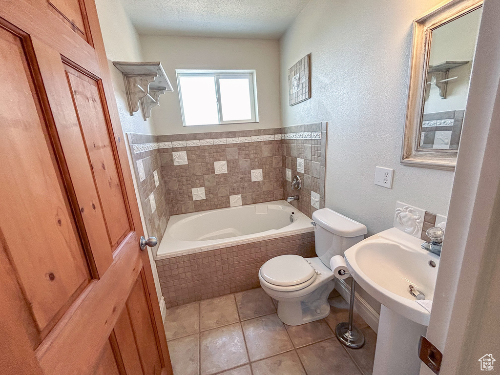 Bathroom featuring toilet, tile floors, a textured ceiling, and tiled tub