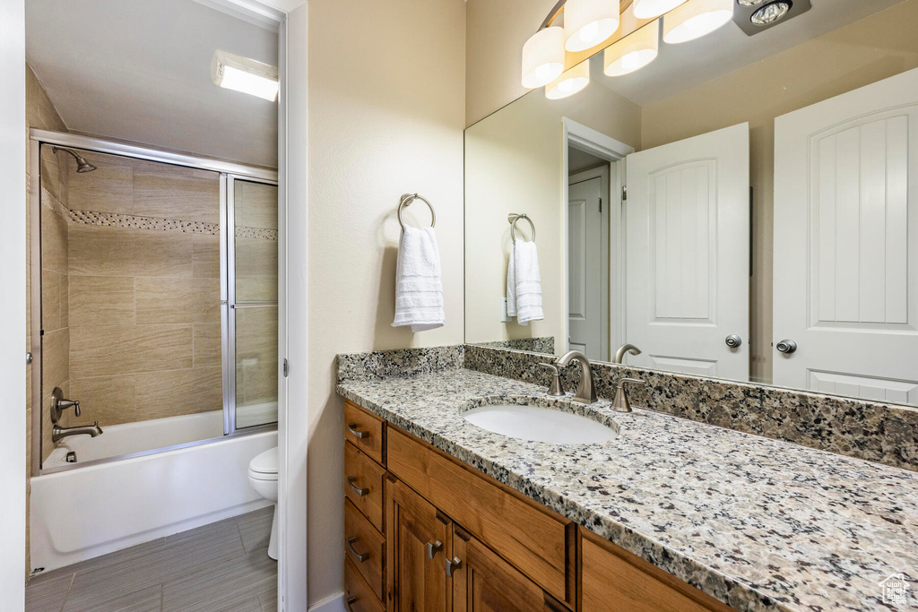 Full bathroom with shower / bath combination with glass door, toilet, tile floors, and vanity with extensive cabinet space
