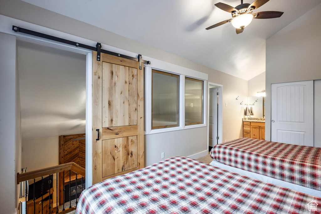 Bedroom with carpet floors, ceiling fan, a barn door, ensuite bath, and lofted ceiling