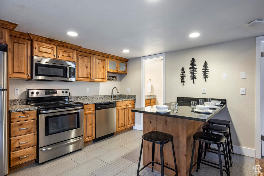 Kitchen featuring dark stone countertops, a breakfast bar, light tile floors, and appliances with stainless steel finishes