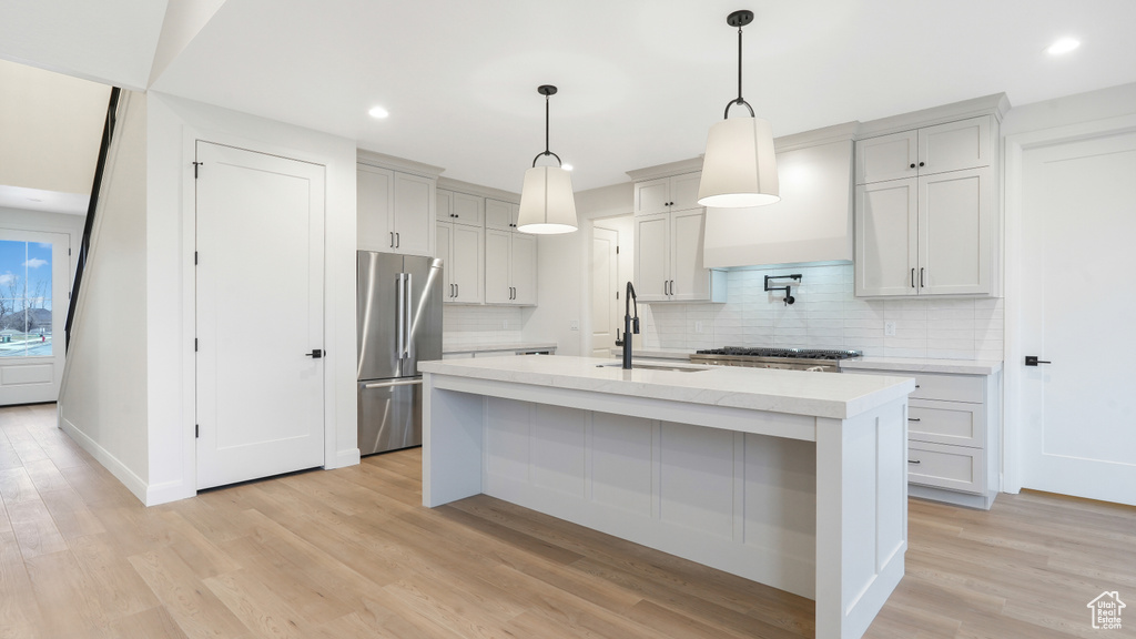 Kitchen featuring tasteful backsplash, a center island with sink, light hardwood / wood-style flooring, high end refrigerator, and hanging light fixtures