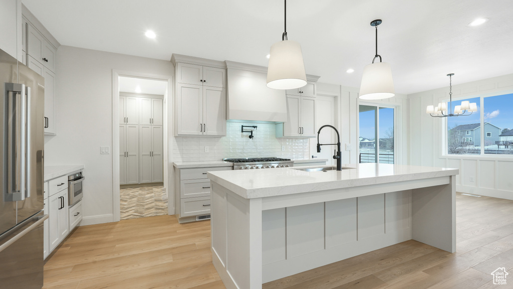 Kitchen featuring premium range hood, light hardwood / wood-style floors, a notable chandelier, hanging light fixtures, and a kitchen island with sink