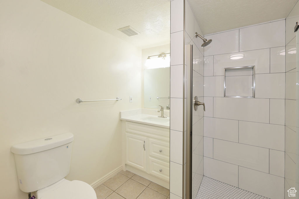 Bathroom featuring tile floors, tiled shower, a textured ceiling, toilet, and oversized vanity