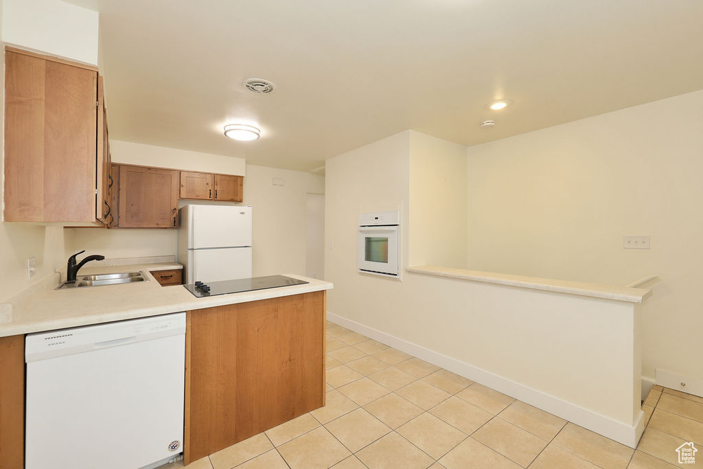 Kitchen featuring white appliances, kitchen peninsula, sink, and light tile flooring