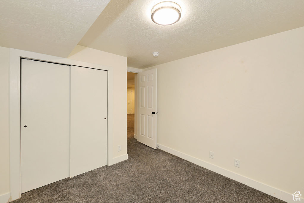 Unfurnished bedroom with a closet, a textured ceiling, and dark colored carpet