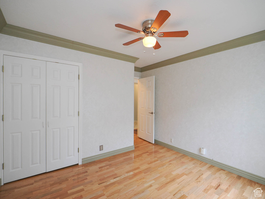 Unfurnished bedroom with crown molding, light hardwood / wood-style floors, a closet, and ceiling fan