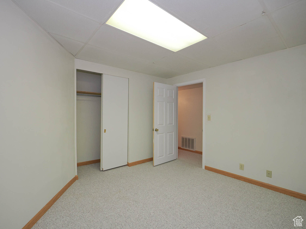 Unfurnished bedroom featuring a paneled ceiling, light colored carpet, and a closet