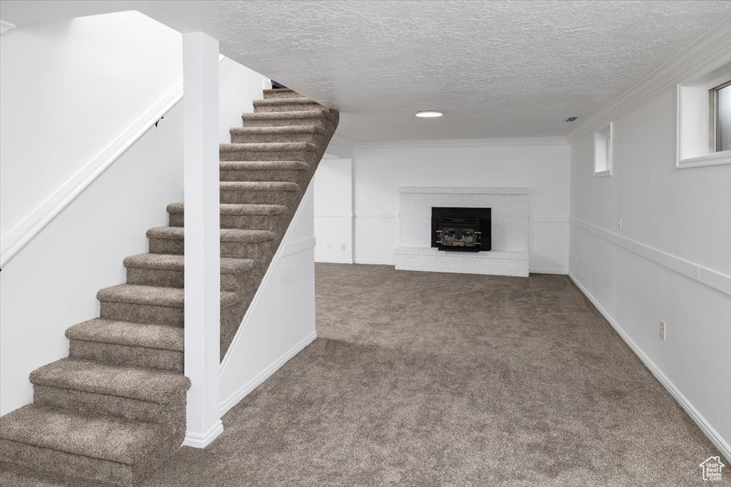 Basement with ornamental molding, a textured ceiling, carpet floors, and a brick fireplace