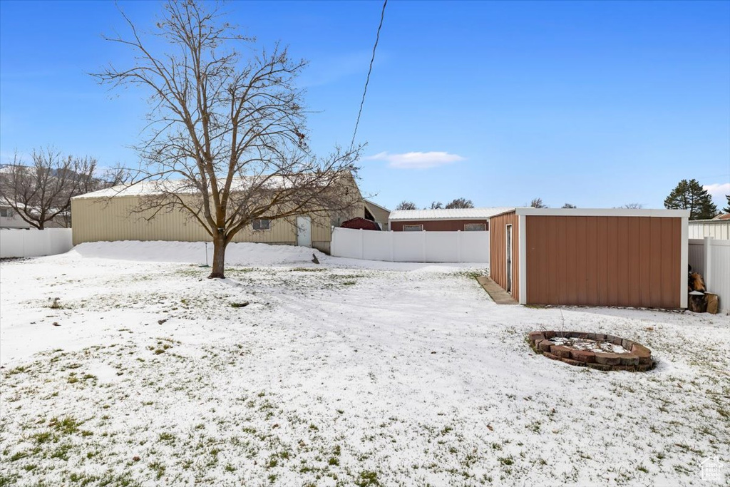 Yard covered in snow with an outdoor fire pit and a shed