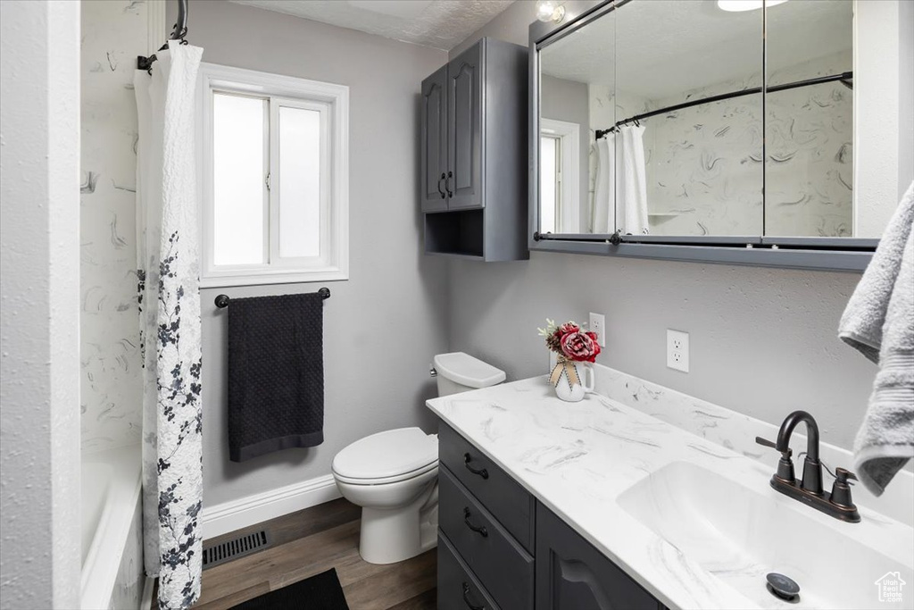 Full bathroom featuring hardwood / wood-style flooring, shower / bath combination with curtain, vanity with extensive cabinet space, and toilet