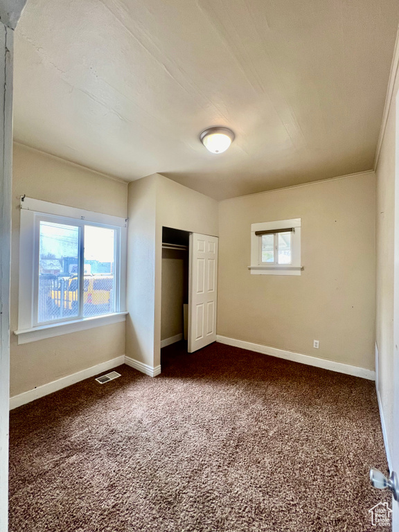 Unfurnished bedroom featuring a closet, dark colored carpet, and multiple windows