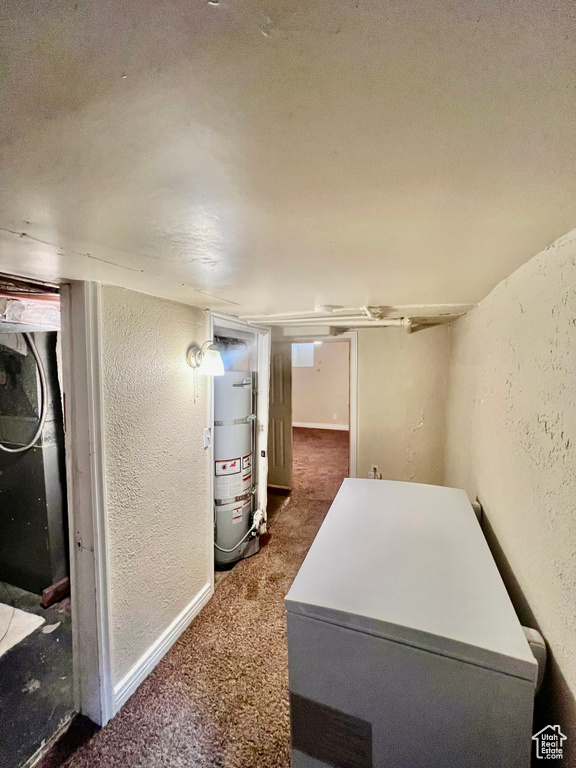 Interior space featuring strapped water heater, a textured ceiling, and dark colored carpet