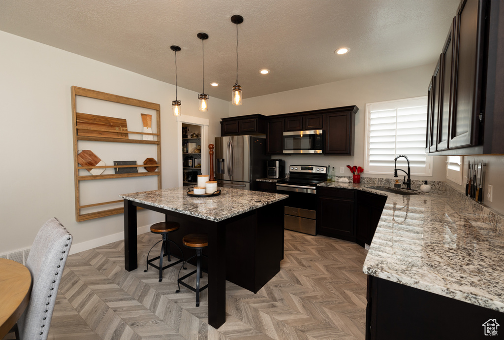 Kitchen with a kitchen breakfast bar, appliances with stainless steel finishes, sink, a kitchen island, and light parquet floors