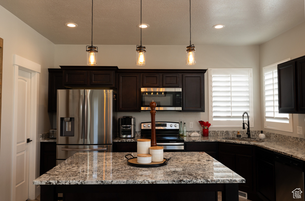Kitchen featuring pendant lighting, a center island, appliances with stainless steel finishes, light stone counters, and sink