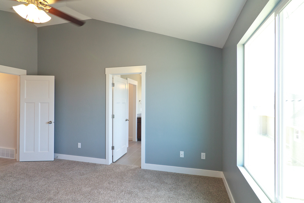 Unfurnished bedroom with ceiling fan, light colored carpet, and vaulted ceiling