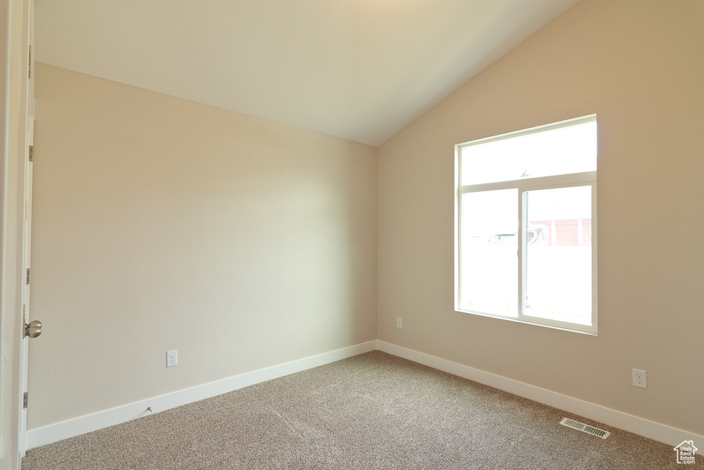 Empty room with light carpet, plenty of natural light, and vaulted ceiling