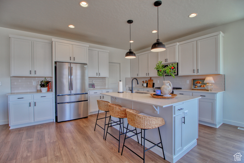 Kitchen featuring tasteful backsplash, stainless steel appliances, white cabinetry, and light wood-type flooring