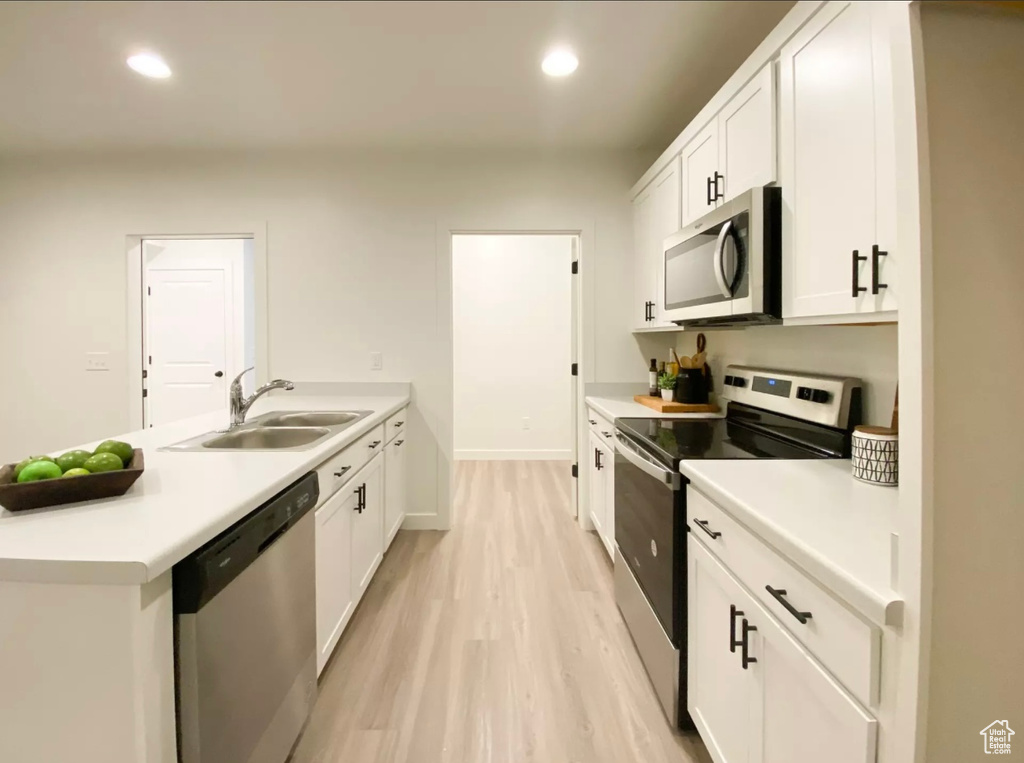 Kitchen with light hardwood / wood-style floors, white cabinets, appliances with stainless steel finishes, and sink