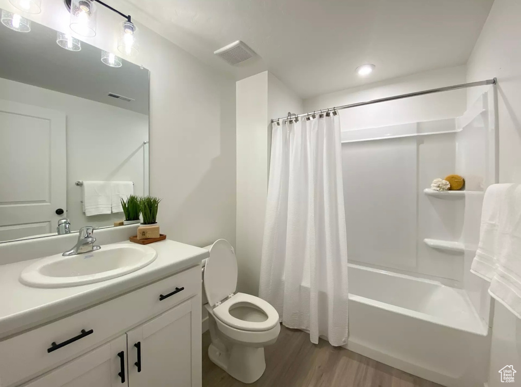 Full bathroom featuring toilet, large vanity, shower / bathtub combination with curtain, and wood-type flooring