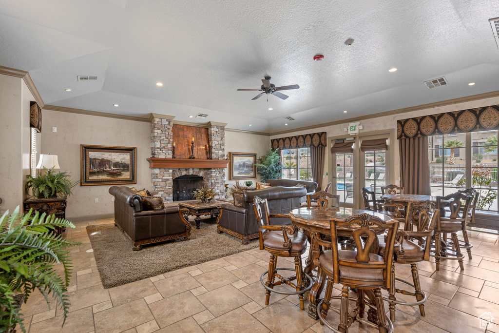 Dining space featuring ceiling fan, light tile floors, a textured ceiling, a stone fireplace, and crown molding