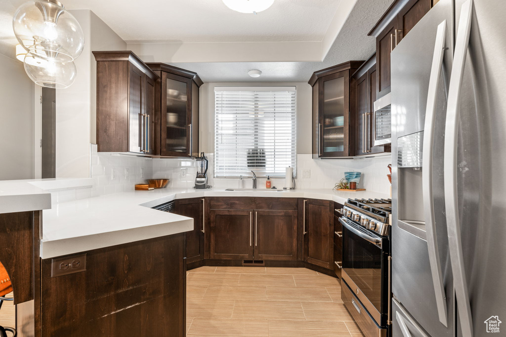 Kitchen with tasteful backsplash, dark brown cabinets, appliances with stainless steel finishes, hanging light fixtures, and sink