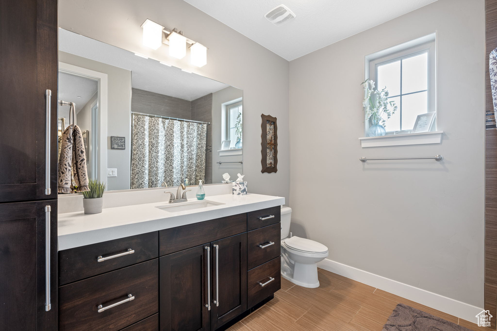 Bathroom featuring a healthy amount of sunlight, vanity with extensive cabinet space, and toilet