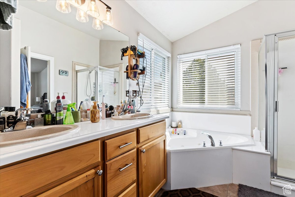 Bathroom with shower with separate bathtub, vanity with extensive cabinet space, dual sinks, vaulted ceiling, and tile flooring