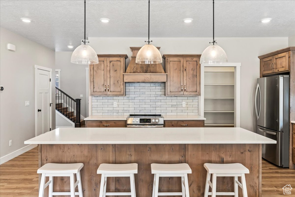 Kitchen featuring appliances with stainless steel finishes, custom range hood, light hardwood / wood-style flooring, and pendant lighting