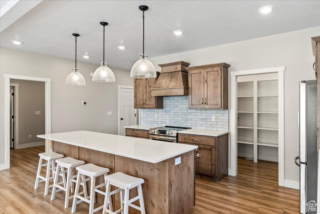 Kitchen featuring light hardwood / wood-style floors, stainless steel appliances, a kitchen island, and custom exhaust hood