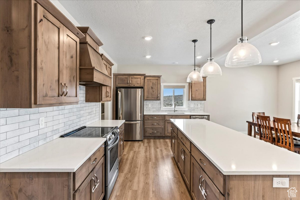 Kitchen featuring stainless steel appliances, a center island, tasteful backsplash, light wood-type flooring, and sink