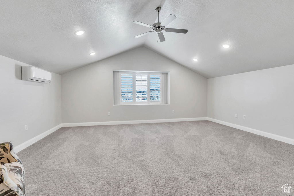 Carpeted spare room featuring lofted ceiling, a wall mounted air conditioner, ceiling fan, and a textured ceiling