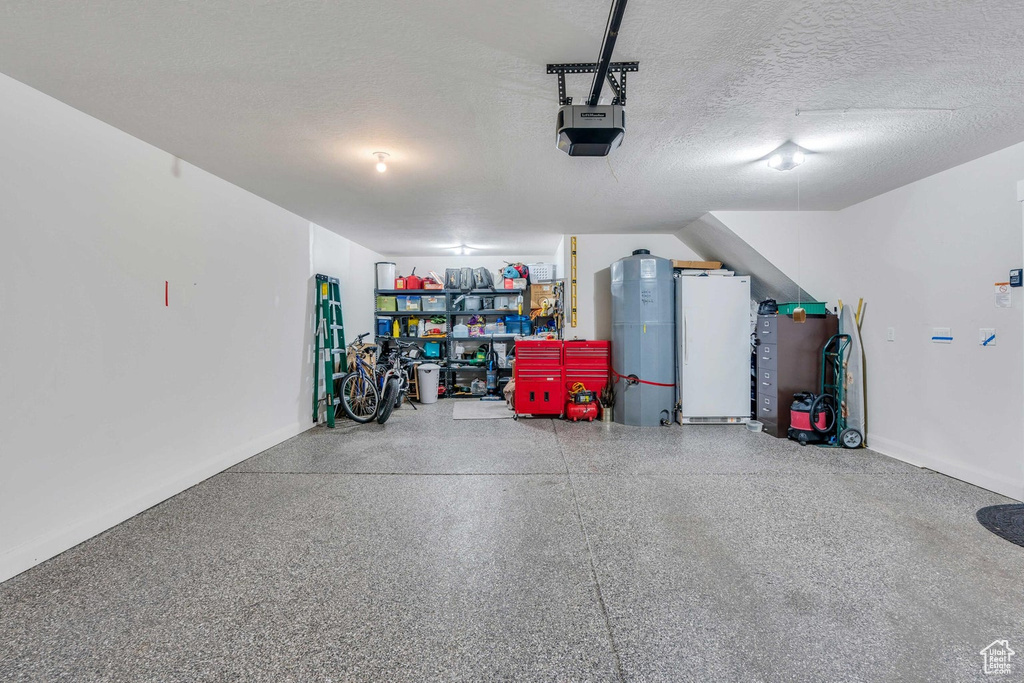 Garage with white refrigerator, water heater, and a garage door opener