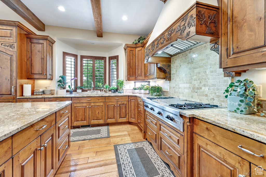Kitchen with backsplash, custom range hood, light wood-type flooring, and light stone counters
