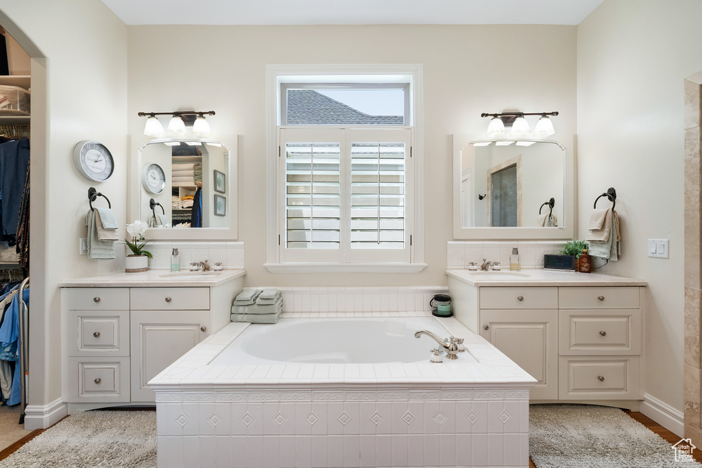 Bathroom featuring tiled bath and dual vanity