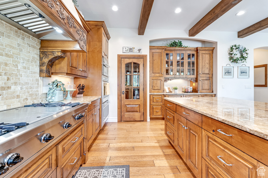 Kitchen with wall oven, light stone counters, custom range hood, light hardwood / wood-style floors, and beam ceiling