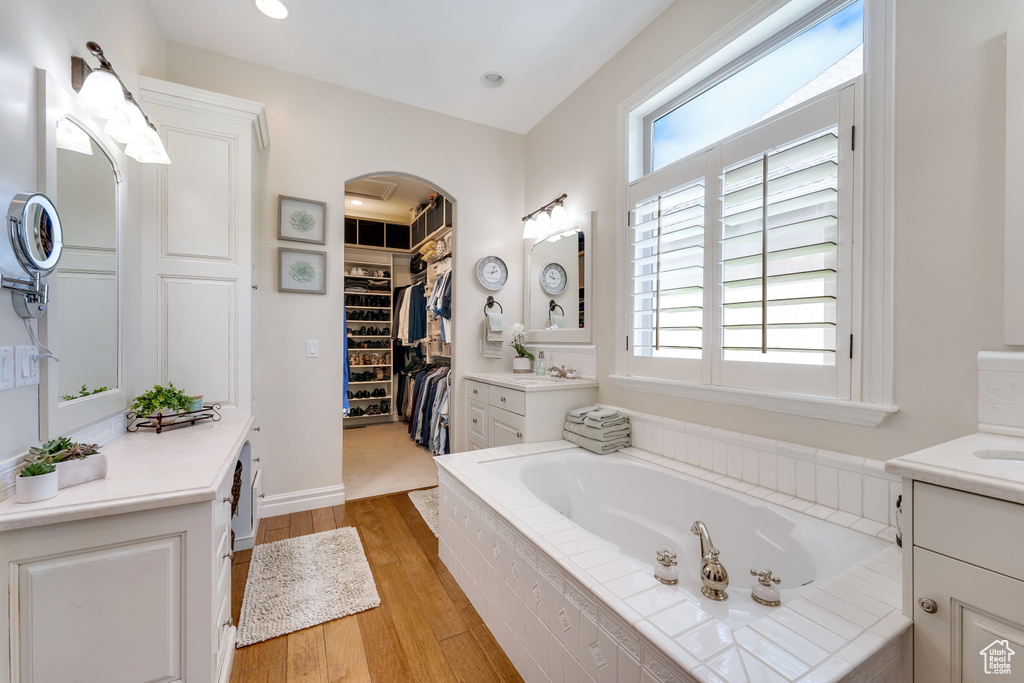 Bathroom with tiled bath, hardwood / wood-style floors, and vanity