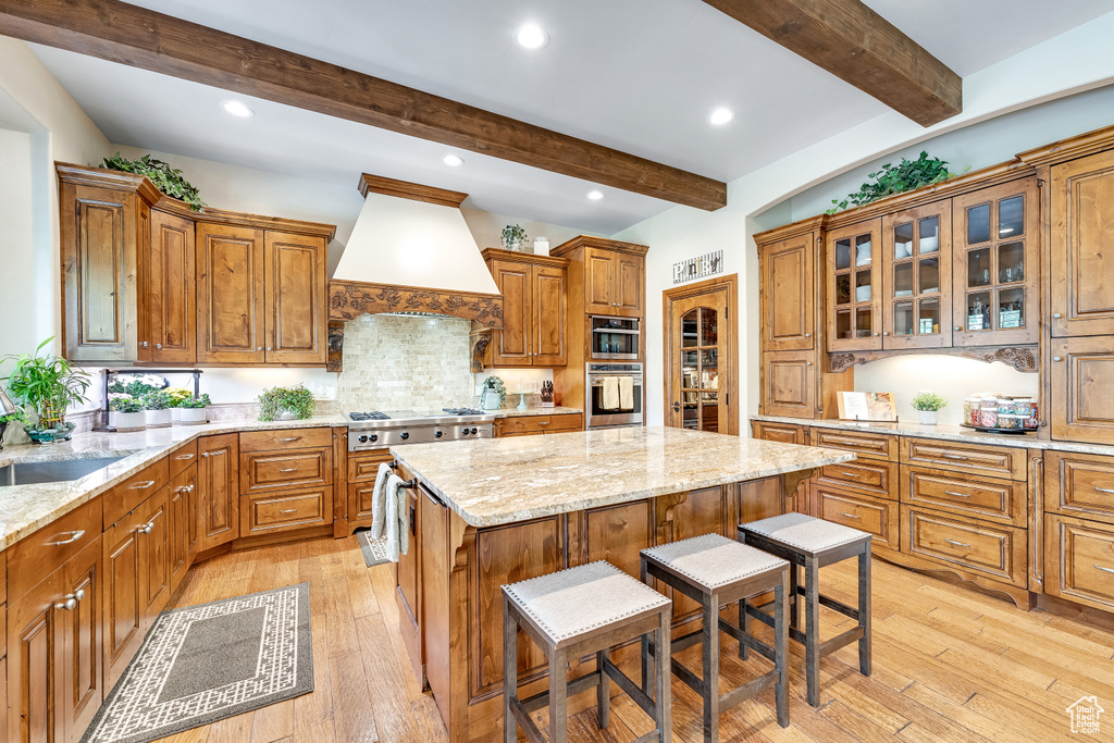 Kitchen with beamed ceiling, light stone counters, and premium range hood