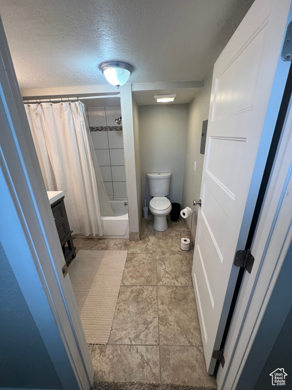 Full bathroom with toilet, shower / tub combo, tile flooring, a textured ceiling, and vanity