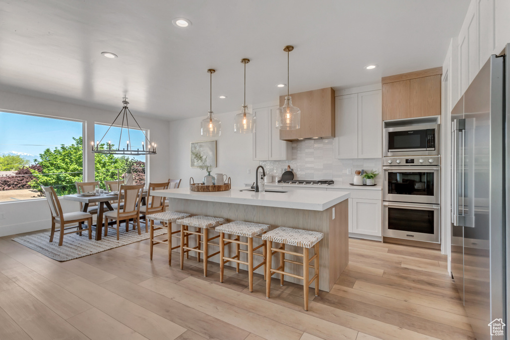 Kitchen featuring decorative light fixtures, a kitchen island with sink, light hardwood / wood-style flooring, stainless steel appliances, and a chandelier